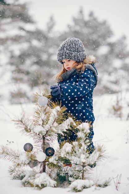 Niña en un sombrero azul jugando en un bosque de invierno