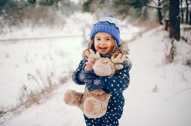 Niña en un sombrero azul jugando en un bosque de invierno