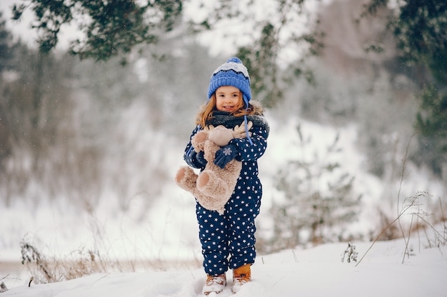 Niña en un sombrero azul jugando en un bosque de invierno