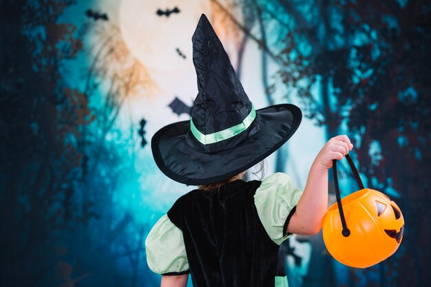 Niña en sombrero de bruja sosteniendo la cesta