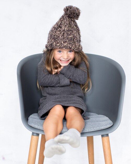 Niña con sombrero de invierno sentado en silla