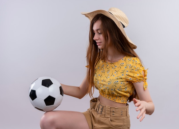 Niña con sombrero jugando con una pelota de fútbol en la pared blanca aislada