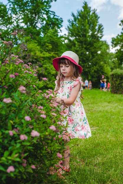 Niña con sombrero mirando las flores de un arbusto