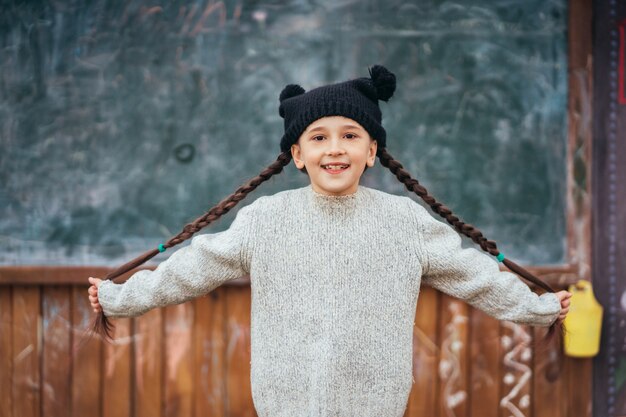 Niña con un sombrero posando delante de una pizarra