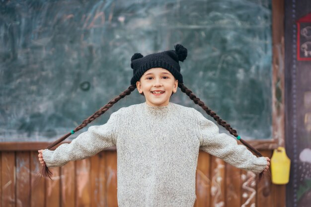 Niña con un sombrero posando en el fondo de la pizarra de la escuela