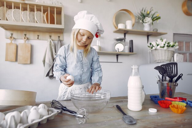 Niña en un sombrero de shef blanco cocinar la masa para galletas