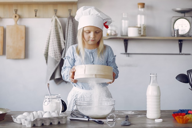 Niña en un sombrero de shef blanco cocinar la masa para galletas