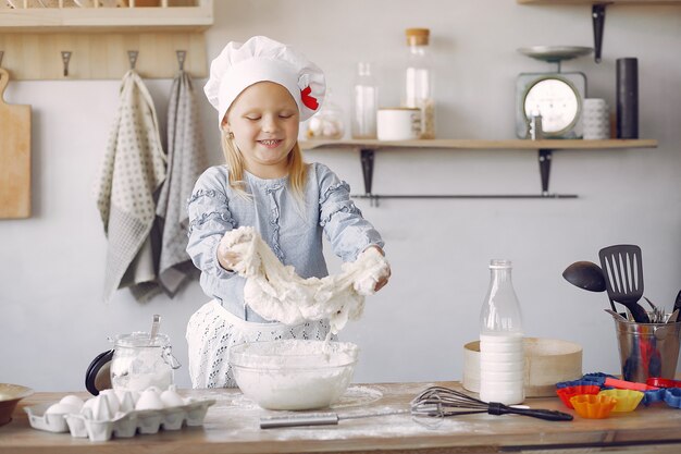 Niña en un sombrero de shef blanco cocinar la masa para galletas