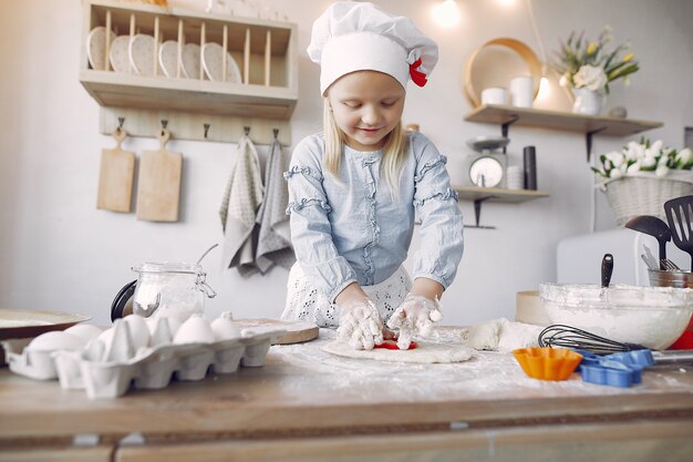 Niña en un sombrero de shef blanco cocinar la masa para galletas