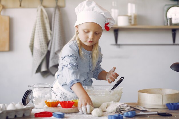 Niña en un sombrero de shef blanco cocinar la masa para galletas