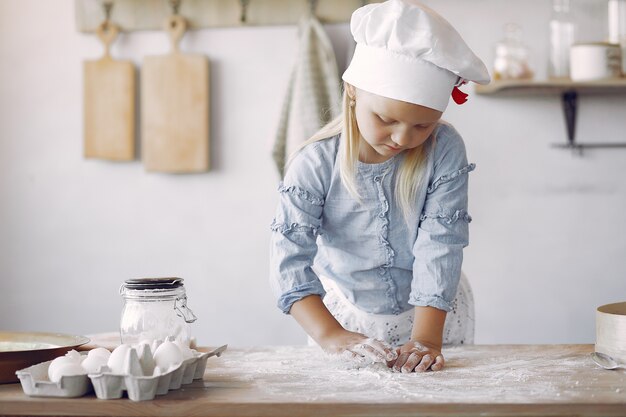 Niña en un sombrero de shef blanco cocinar la masa para galletas