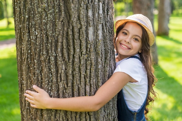 Niña sonriente abrazando un árbol