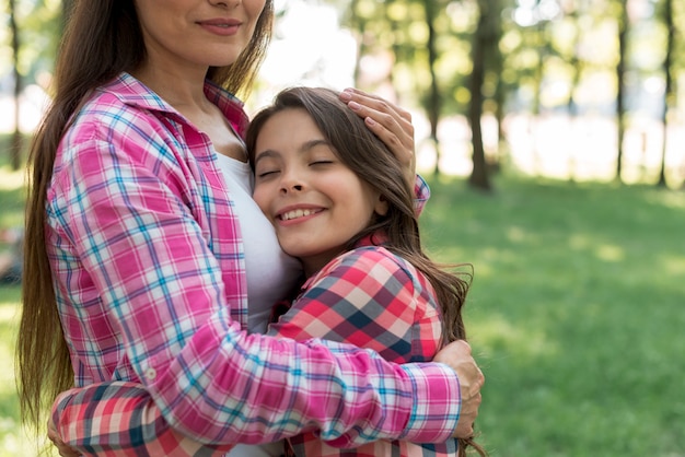 Foto gratuita niña sonriente abrazando a su madre con los ojos cerrados en el jardín