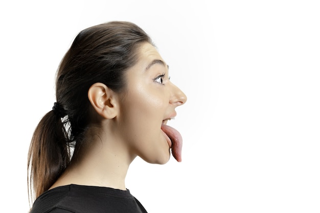 Niña sonriente abriendo la boca y mostrando la lengua gigante grande y larga aislada en la pared blanca. Parece sorprendido, atraído, asombrado y asombrado. Copyspace para anuncio. Emociones humanas, marketing.