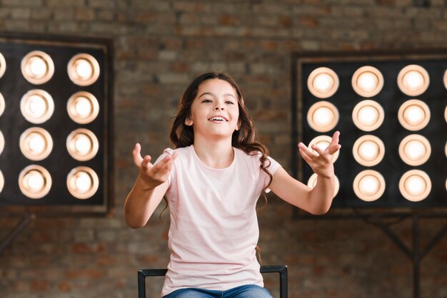 Niña sonriente actuando en estudio con luz de escenario en el fondo