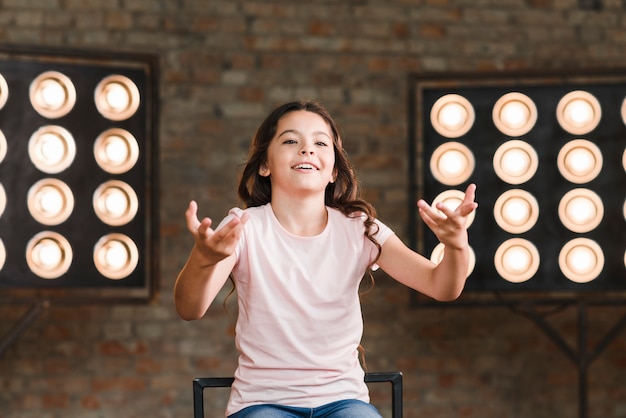 Niña sonriente actuando en estudio con luz de escenario en el fondo