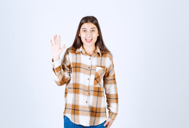 niña sonriente agitando una mano en la pared blanco-gris.