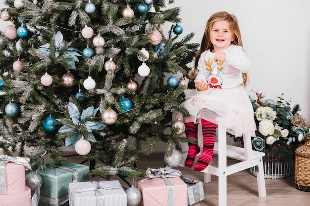 Niña sonriente al lado de árbol de navidad