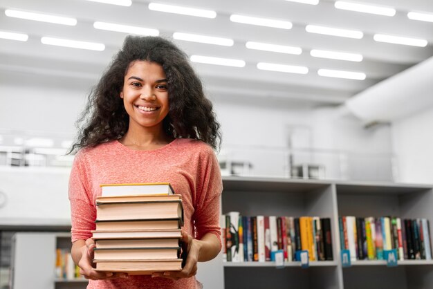 Niña sonriente de ángulo bajo con pila de libros