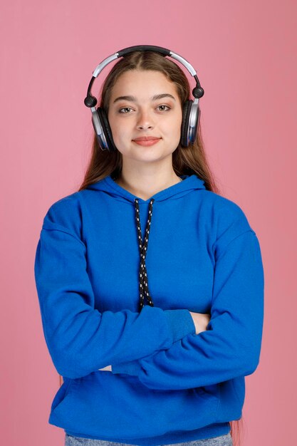 Niña sonriente con auriculares escuchando música mientras mantiene los brazos cruzados y mira la cámara