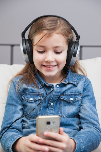 Niña sonriente en auriculares, navegación por teléfono inteligente