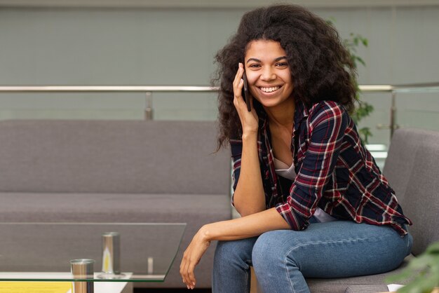 Niña sonriente en la biblioteca hablando por teléfono