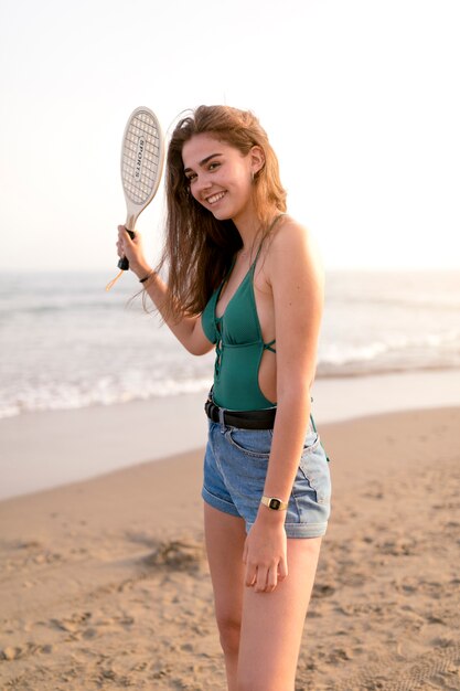 Niña sonriente en bikini verde jugando al tenis en la playa