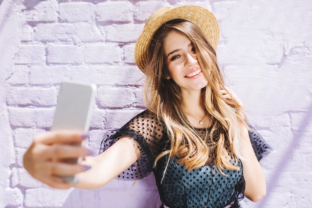 Foto gratuita niña sonriente con cabello brillante disfrutando del buen tiempo durante la caminata y haciendo selfie