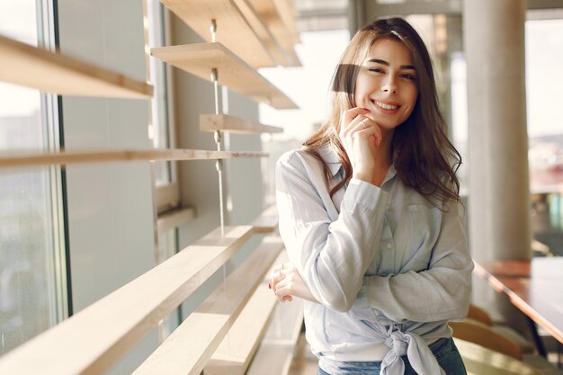 Niña sonriente en una camisa azul de pie junto a la ventana y posando