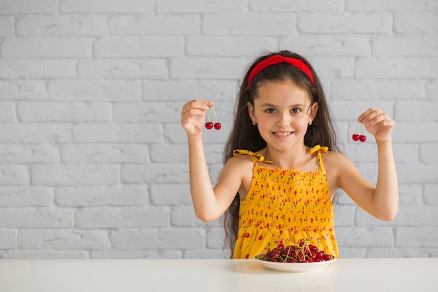 Niña sonriente con cerezas rojas en la mano