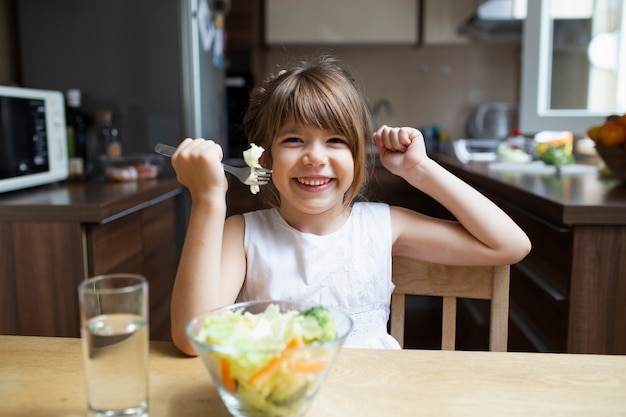 Niña sonriente comiendo ensalada con cubiertos