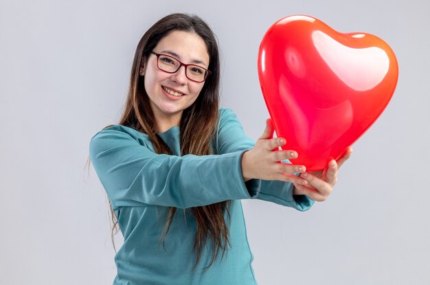 Niña sonriente en el día de San Valentín sosteniendo el globo del corazón en la cámara aislada sobre fondo blanco.