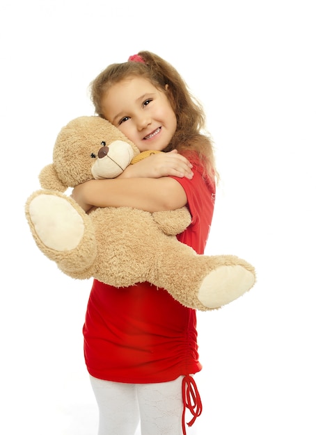 Niña sonriente está abrazando con oso en vestido rojo aislado en blanco