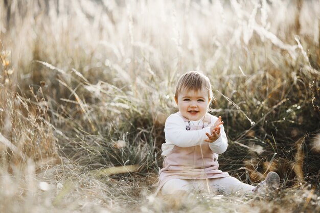 Niña sonriente está sentada en el césped a la luz del sol