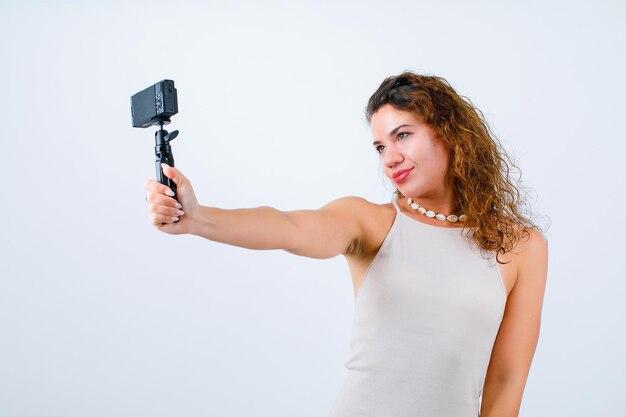 Niña sonriente está tomando selfie con su mini cámara sobre fondo blanco.