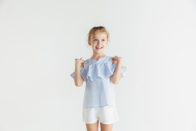 Niña sonriente con estilo posando en ropa casual aislado en la pared blanca. Modelo de mujer rubia caucásica. Emociones humanas, expresión facial, infancia. Mostrar, invitar o saludar.