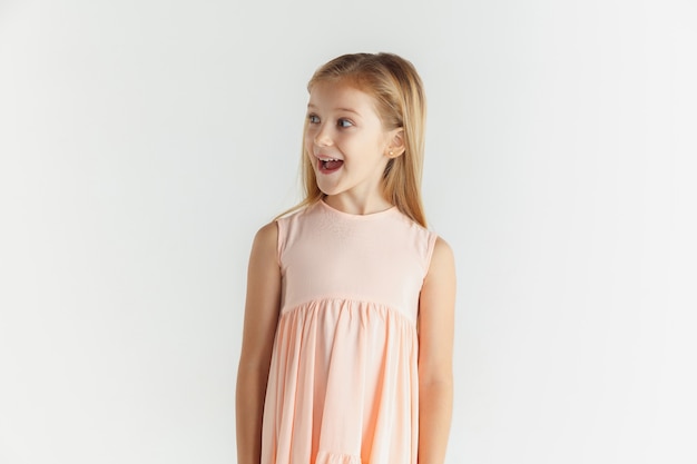 Niña sonriente con estilo posando en vestido aislado sobre fondo blanco de estudio. Modelo de mujer caucásica. Emociones humanas, expresión facial, infancia. Maravillada, asombrada, conmocionada. Mirando de lado.