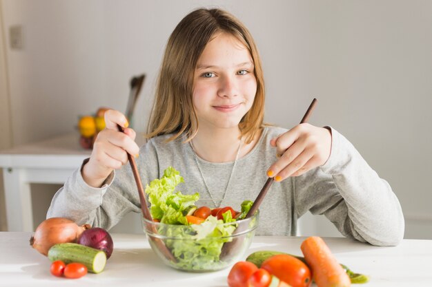 Niña sonriente haciendo ensalada de vegetales saludables