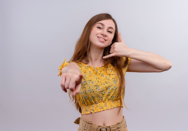 Niña sonriente haciendo gesto de llamada y apuntando a una pared blanca aislada con espacio de copia