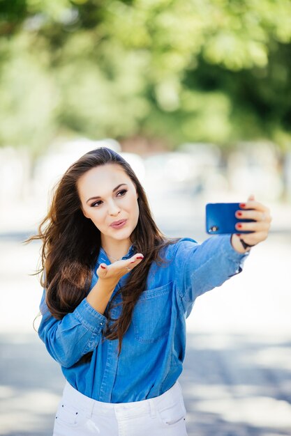 Niña sonriente haciendo selfie enviar besos en el fondo de la ciudad