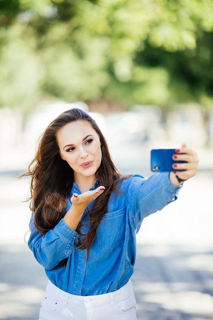 Niña sonriente haciendo selfie enviar besos en el fondo de la ciudad