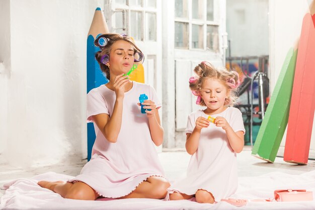 Niña sonriente jugando con burbuja y su madre en blanco