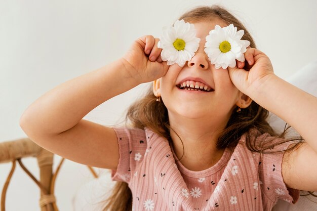 Niña sonriente jugando con flores de primavera cubriendo sus ojos