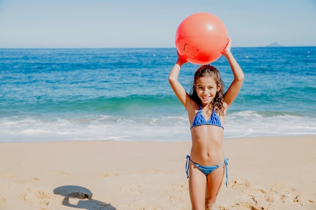 Foto gratuita niña sonriente jugando con pelota en la playa