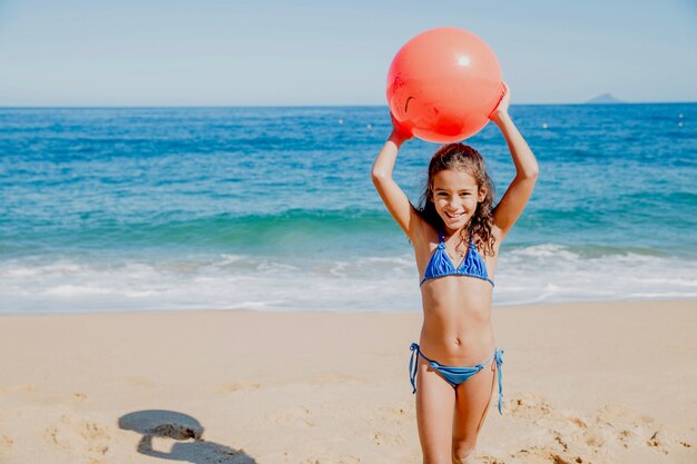 Niña sonriente jugando con pelota en la playa