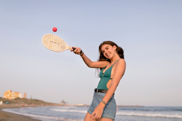 Niña sonriente jugando con pelota de tenis y raqueta en la playa