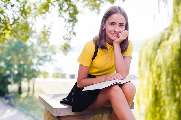 Niña sonriente con el libro en el parque