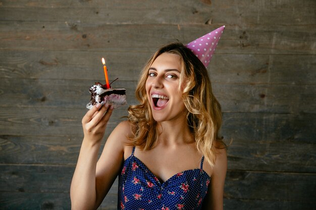 Niña sonriente, lista para comer un pedazo de pastel de chocolate con vela, con sombrero festivo.