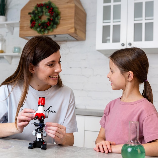 Niña sonriente y madre haciendo experimentos con microscopio