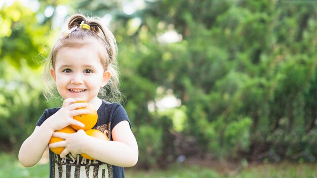 Niña sonriente con naranjas frescas en el parque